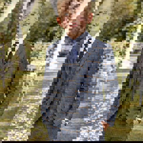 Young boy in a blue checkered suit standing outdoors with floral decorations.