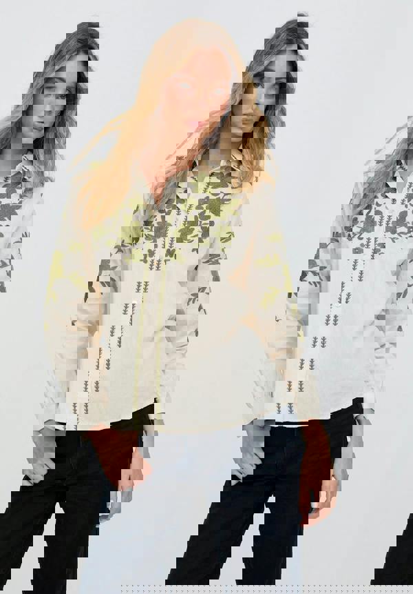 Woman wearing a cream blouse with green floral patterns on a white background