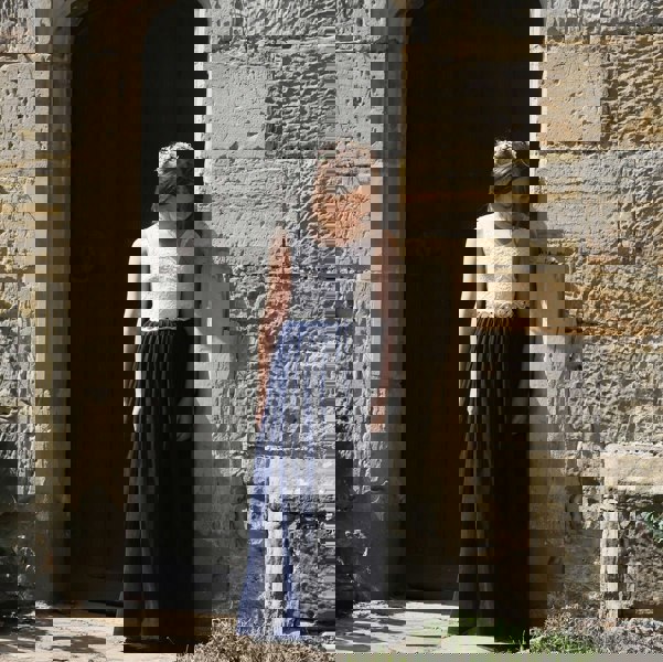 Girl in a white top and navy blue skirt standing against a stone wall.