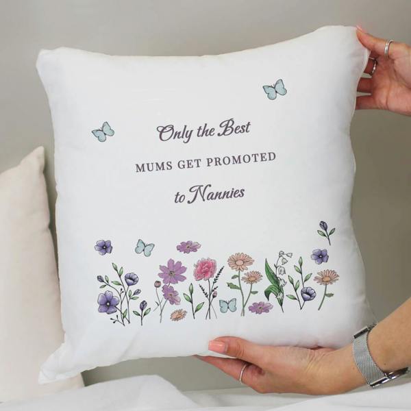 A person holding a white personalised cushion printed with a wildflower design and the words 'Only the Best Mums get promoted to Nannies'.