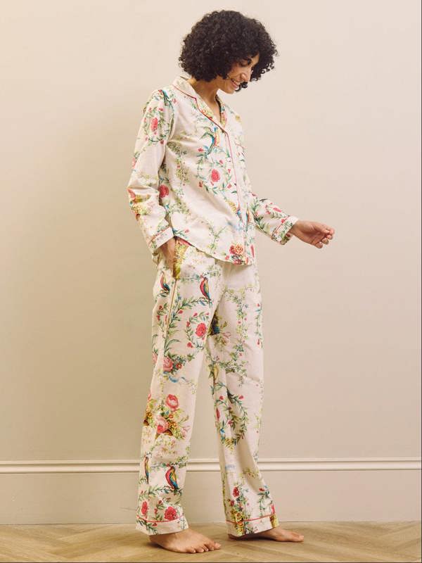 Woman wearing floral pyjamas standing against a plain wall.