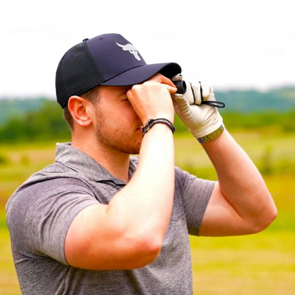 A golfer wearing a glove and cap uses the golf distance finder to gauge range on the course, demonstrating the accessory's use.