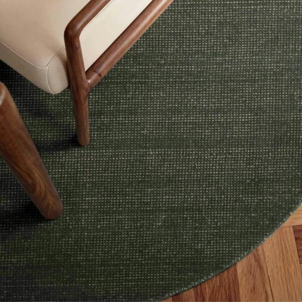 Round dark green rug on a wooden floor with a chair corner.