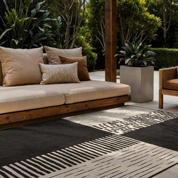 Outdoor seating area with a beige sofa and patterned rug on a patio.