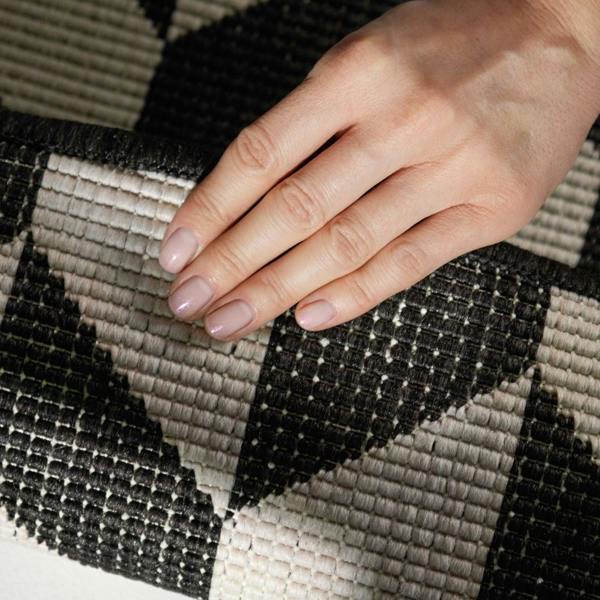 Hand with light pink nail polish on a textured surface