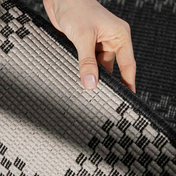 Hand holding a corner of a textured black and beige rug