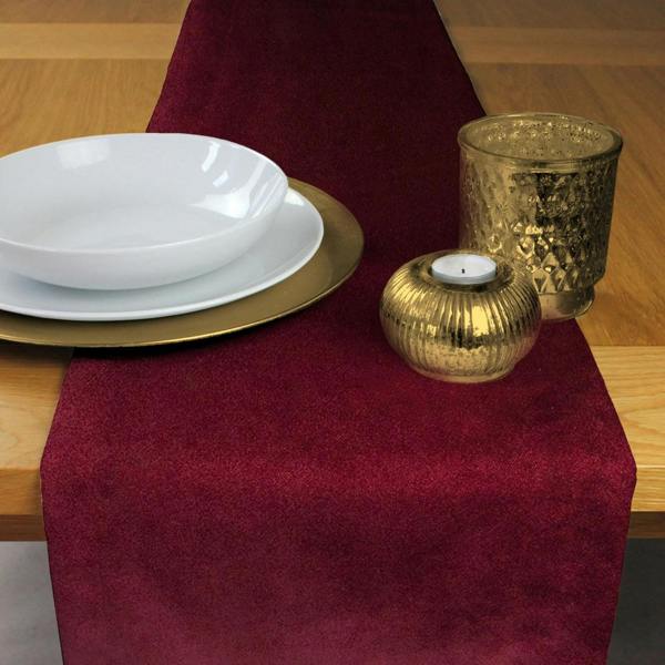 Luxury wine red matt velvet table runner styled with gold candle holders and white dinnerware on a wooden table.
