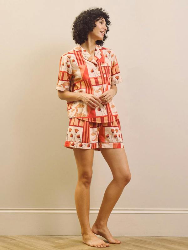 Woman wearing a rust and cream patch work patterned pyjama set against a plain wall.
