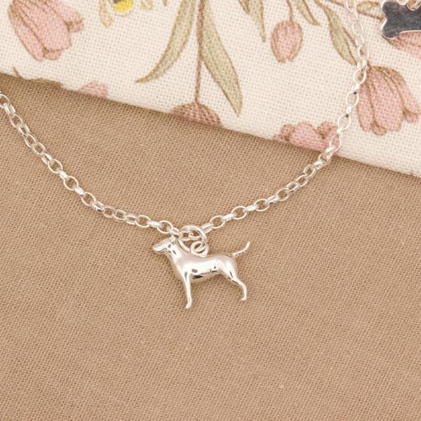 Silver bull terrier dog-shaped charm on a chain against a floral fabric background