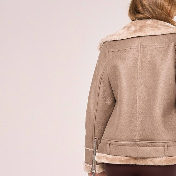 Image displays the back of a faux fur aviator jacket by Barneys Originals. It is beige in colour and you can see the adjustable belt runs around the back of the jacket.