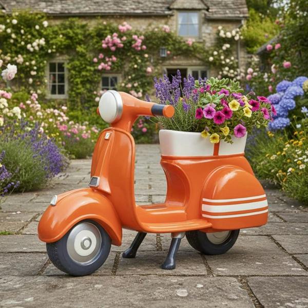 A vibrant orange retro scooter planter filled with purple lavender and pink flowers, displayed on a stone garden path outside a cottage.