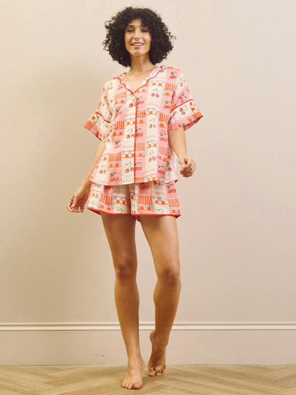 Woman wearing a cherry patterned pyjama set against a plain background