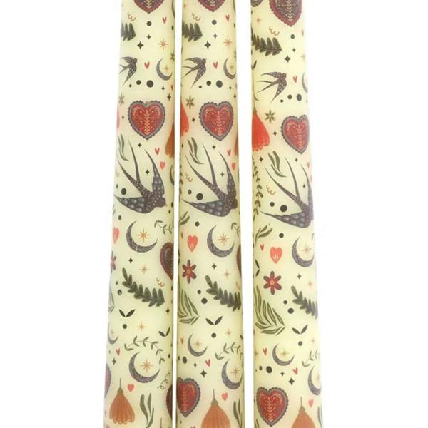 Close view of three cream taper candles with hearts, birds, and crescent moon print