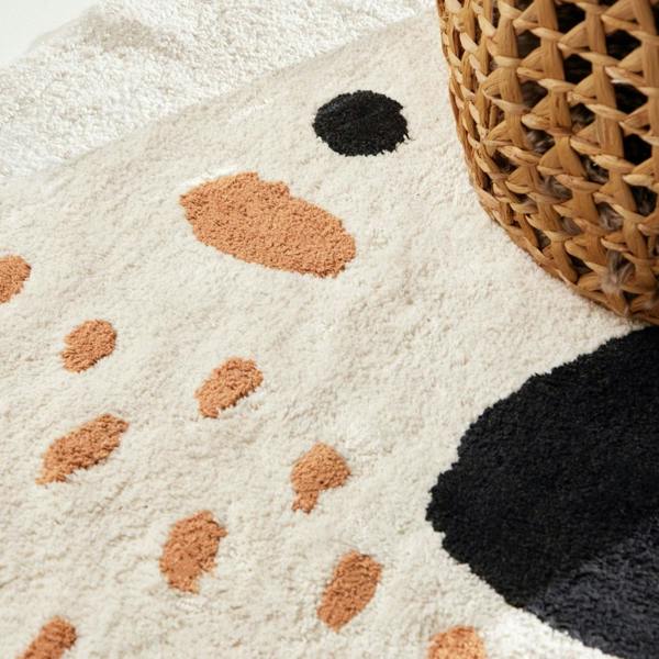Close-up of a textured rug with brown and black abstract patterns next to a woven basket.