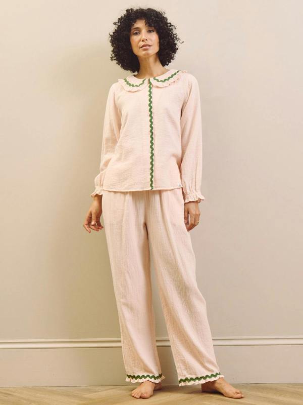 Woman wearing a pink pyjama set with green trim against a beige wall.