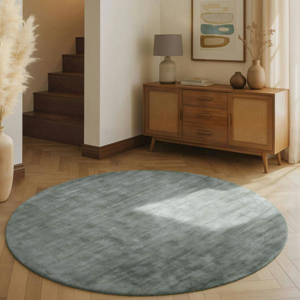 Round gray rug on a wooden floor with a wooden sideboard and decorative items in the background.