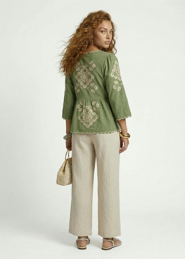 Woman wearing a green embroidered top and beige pants on a white background