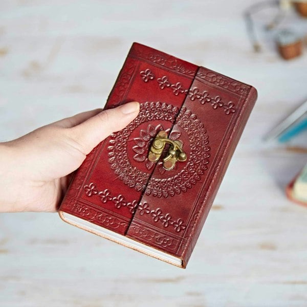 A person holding an Indra Medium Embossed Leather Journal with an ornate design.