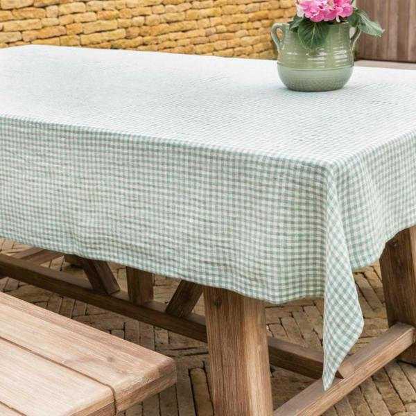 A rosemary green and white gingham linen tablecloth styled on a wooden garden table with a green vase and pink flowers.