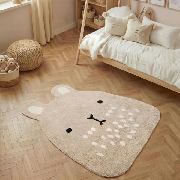 Children's room with a bear-shaped rug on a wooden floor, bed with pillows, and toys.