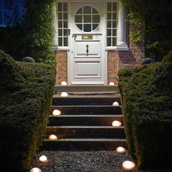 Multiple frosted glass solar pebble lights illuminating a gravel path and brick steps leading up to a white front door at night.
