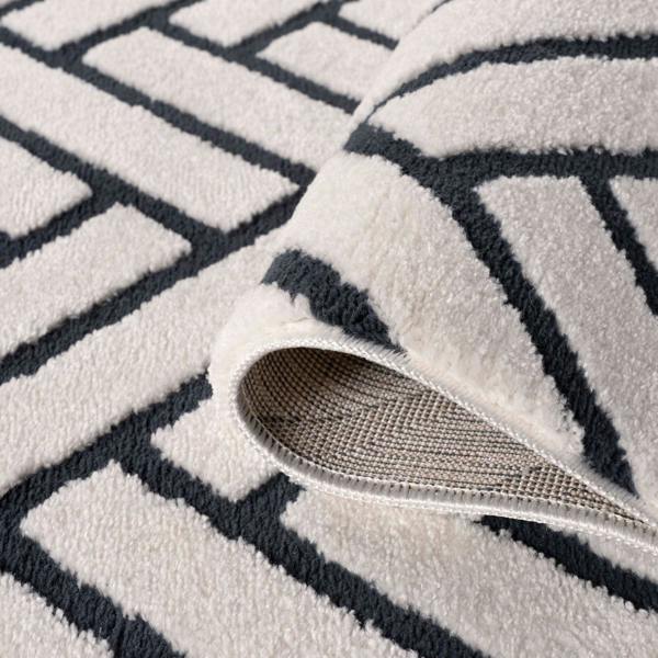 Close-up of a textured rug with geometric pattern and a part of a shoe visible.