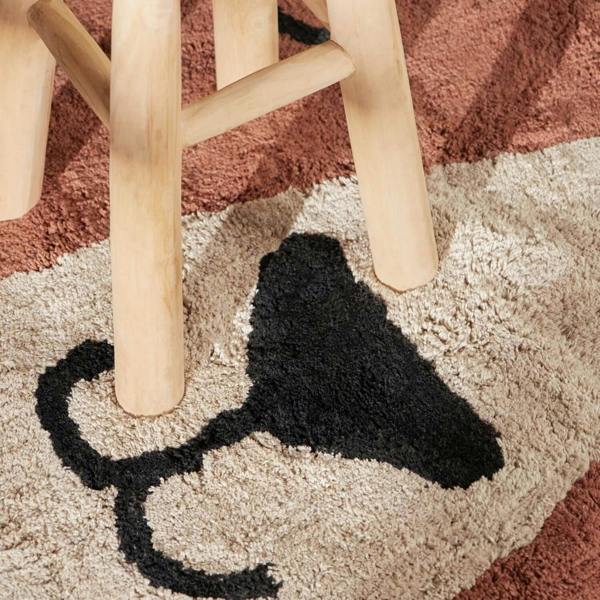 Black shoe on a patterned carpet with wooden legs of a chair visible