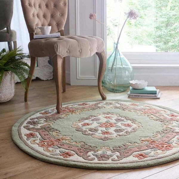 Round floral rug on a wooden floor with a chair and decor items in the background.
