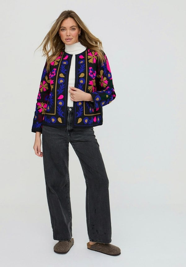 Woman wearing a colorful embroidered jacket on a white background