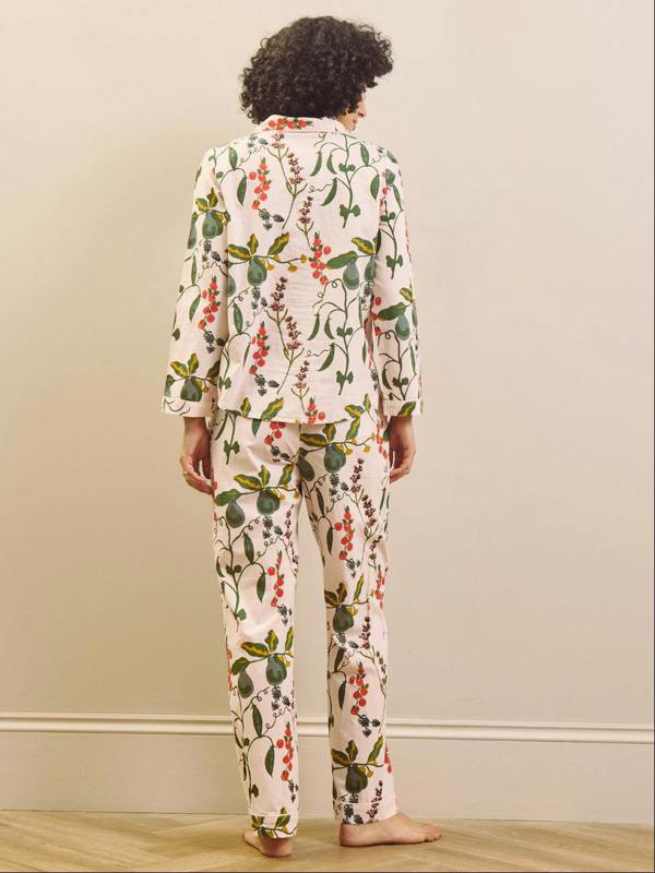 Woman wearing a pear & floral pyjama set against a plain wall.