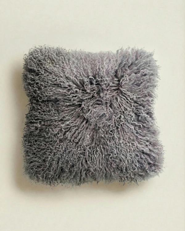 Fluffy grey mongolian sheepskin pillow on a beige background