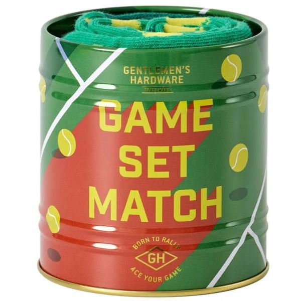 An open cylindrical metal storage tin featuring 'Game, Set, Match' typography, filled with a neatly rolled pair of green tennis socks.