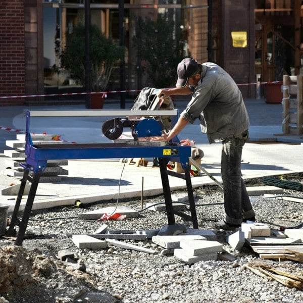 T-Mech Wet Tile Cutter Bench in use, featuring a blue frame, 1200mm cutting surface, and a worker cutting tiles on a construction site