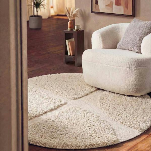 Round beige rug in a living room with a white armchair and side table.