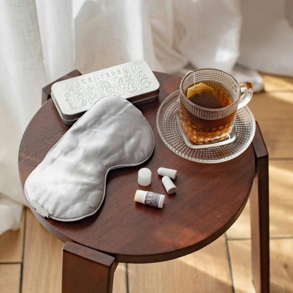 Goodnight Gift Set with Silk eye mask, Sleep Well Mini balm and ear plugs laid out on table next to a cup of herbal tea
