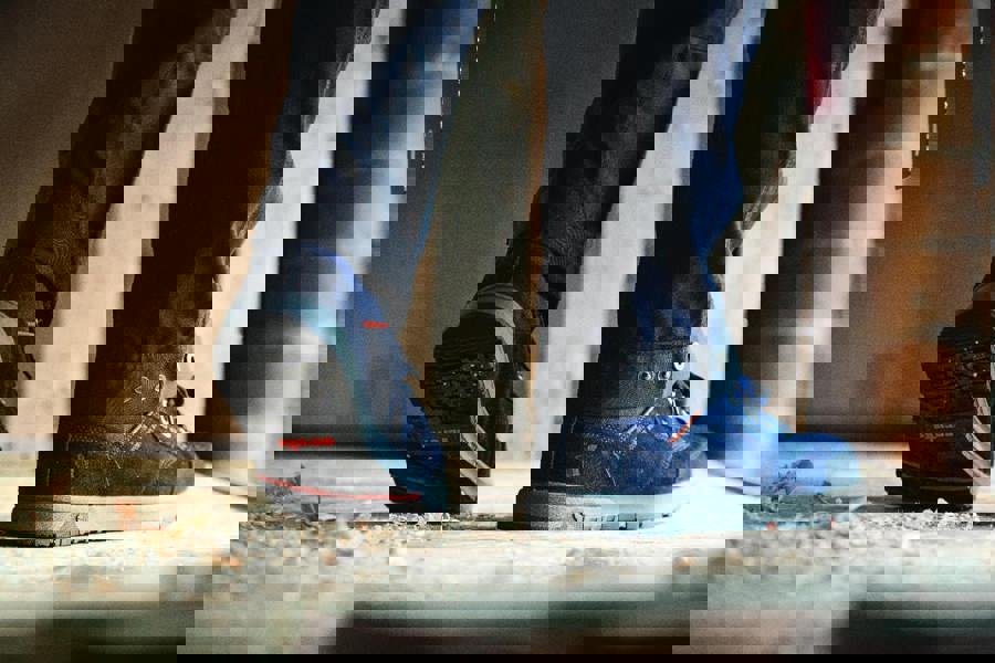 Scruffs Halo 3 Mens Safety S3 Lace Up Steel Toe Midsole Trainers, close-up of blue safety shoes worn by a person standing on a wooden floor.