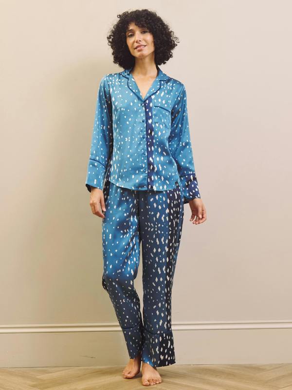 A woman modelling a two-piece pyjama set with a blue and white abstract fawn pattern, standing against a beige wall on a light wood floor.