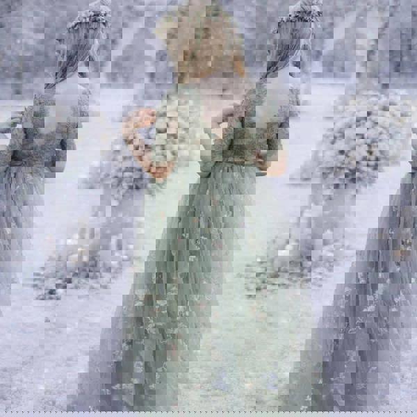 Woman in a green floral dress standing in a snowy landscape with floral arrangements.