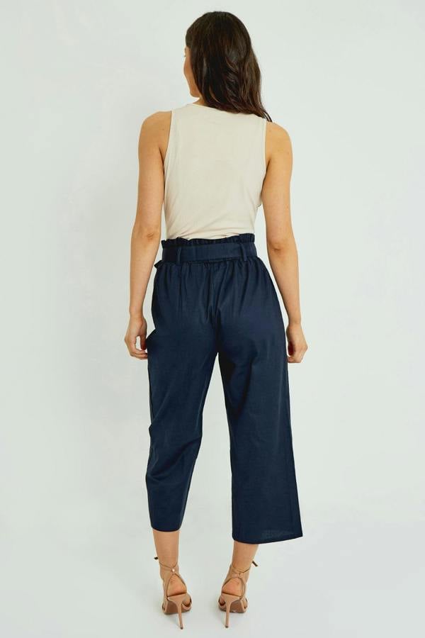 Woman wearing navy pants and a beige top on a white background