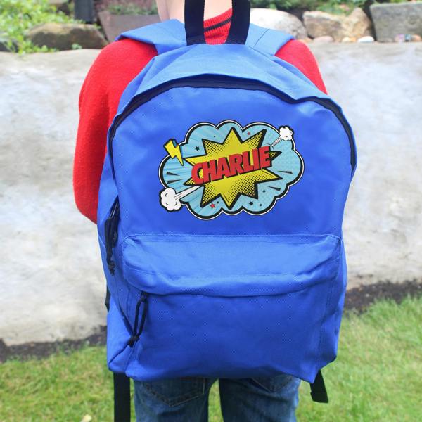 A child wearing a red sweater wears a personalised blue backpack featuring a yellow and red comic book action burst graphic and the name CHARLIE.