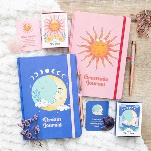 Pink gratitude journal with sun cover and red ribbon spine, with rose quartz pen nearby