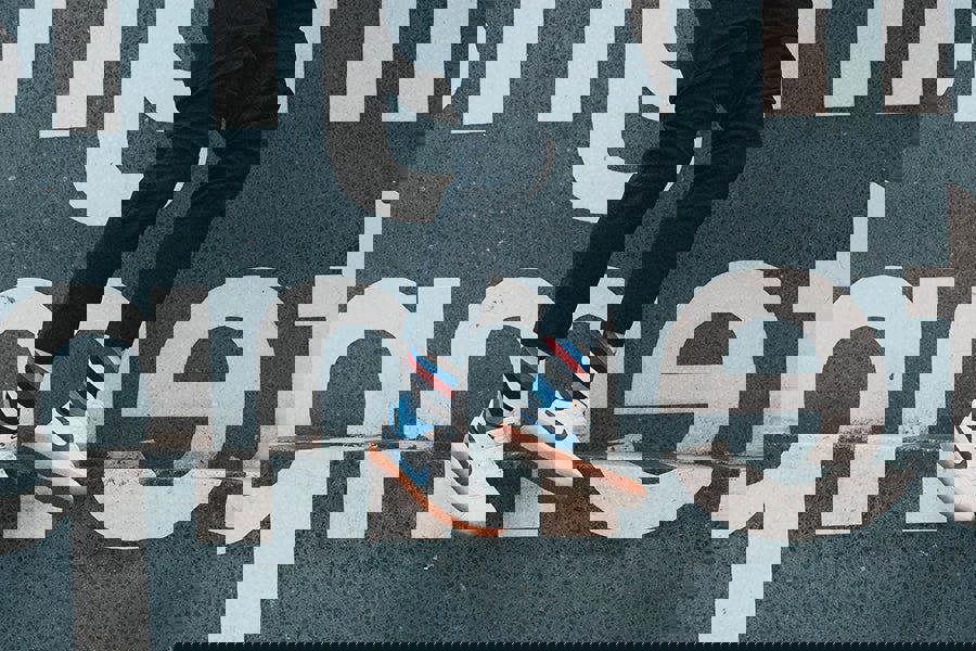 Person wearing striped socks and white sneakers with blue accents, standing on a street sign.