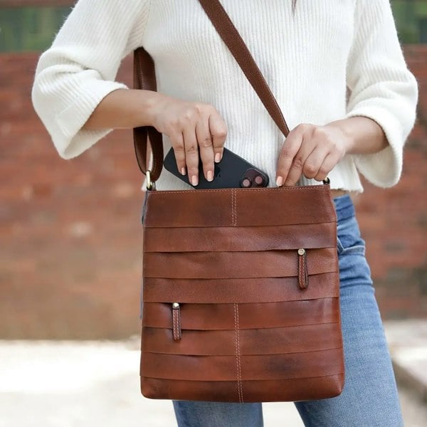 Close-up of a woman placing a smartphone into the spacious main compartment of the Boho Layered Leather Bag - Ridgeback, highlighting its functional storage and premium leather craftsmanship.