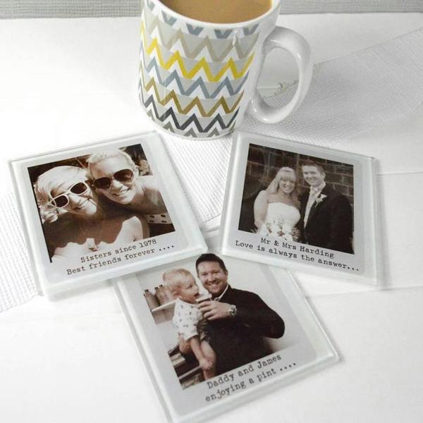 Three square glass coasters personalised with black and white family photos and custom text captions next to a patterned coffee mug.