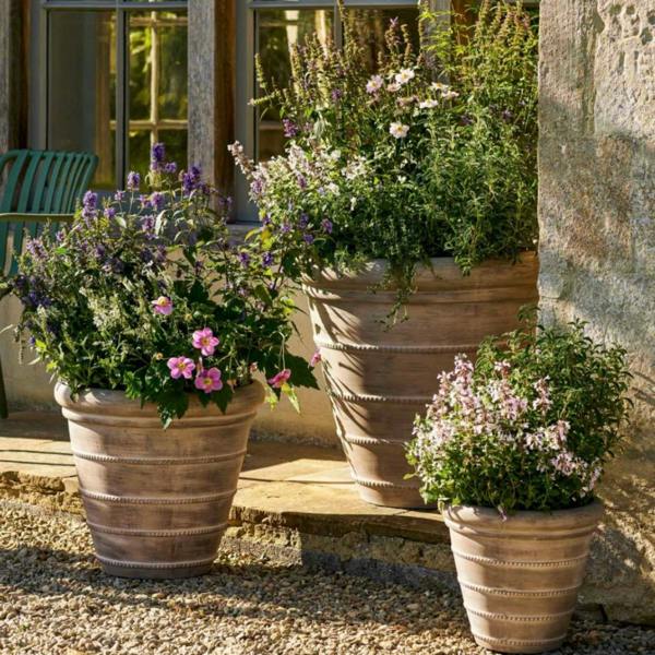 Small 36cm Cotswold ribbed terracotta planter shown clustered in a tiered display with its medium and large matching pots on a gravel patio.