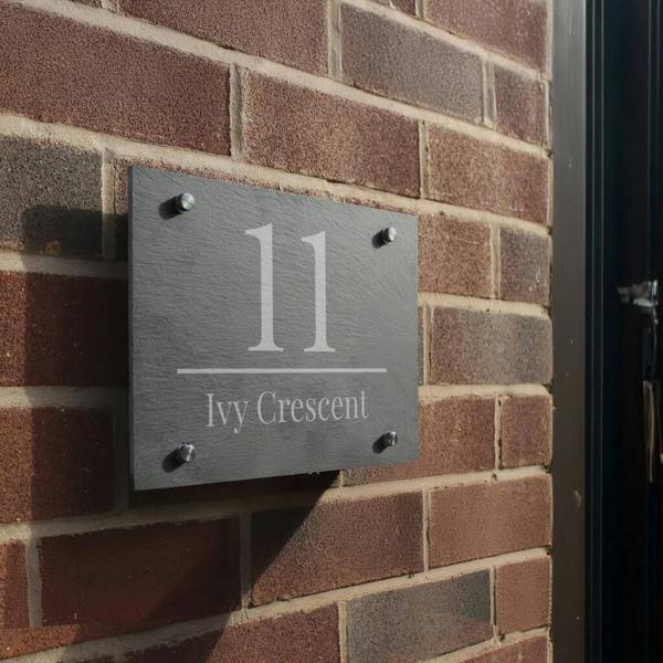 A rectangular dark grey slate house sign mounted on a brick wall, engraved with the number "11" and the text "Ivy Crescent".