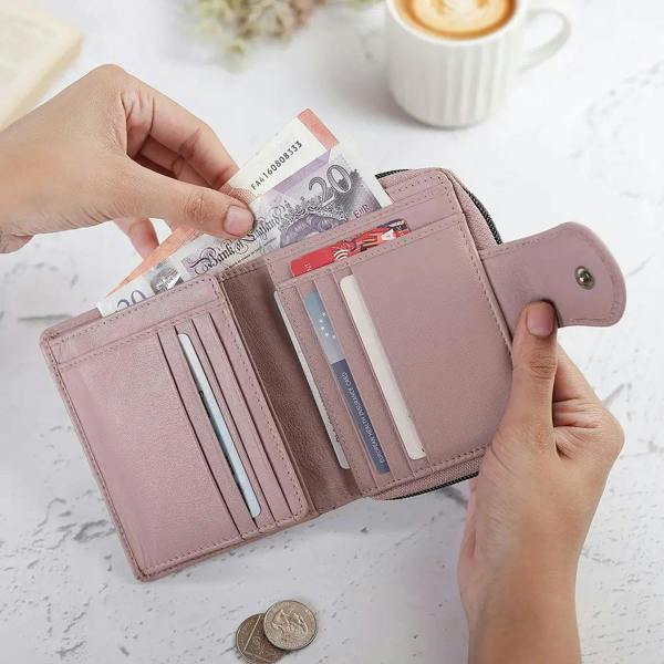 Pink wallet with cards and money held by hands on a light surface with a blurred coffee cup in the background