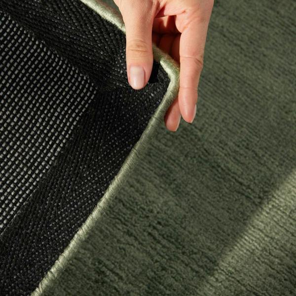 Hand holding a green rug edge with a black textured area
