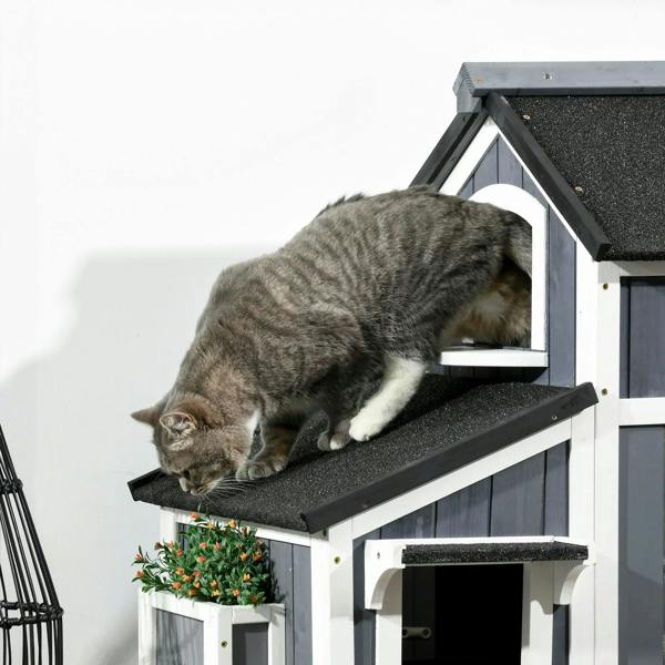 Grey tabby cat resting on the top platform of a grey wooden cat house