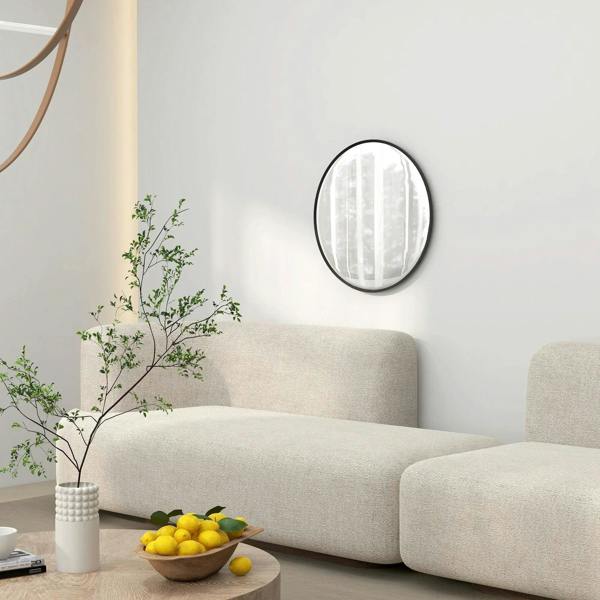 Round black wall mirror with thin frame above a sofa, reflecting window light